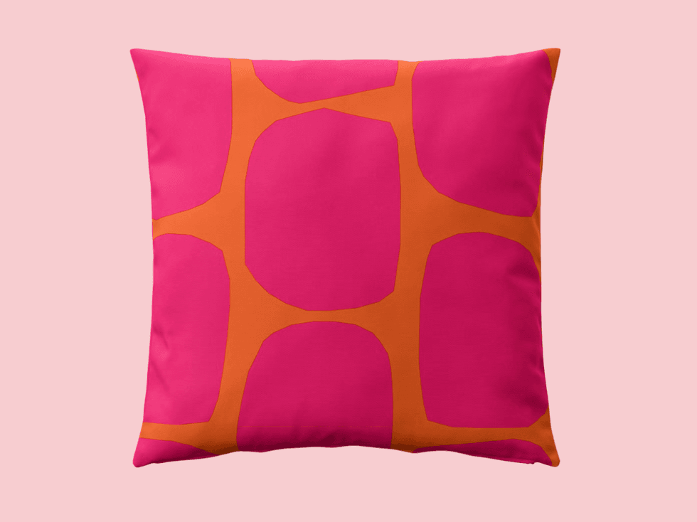 Bright pink pillow with bold orange geometric pattern on a light pink background.
