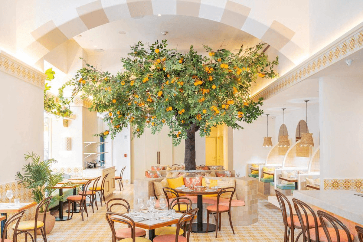 Bright restaurant with orange tree décor, wooden chairs, and patterned floor tiles.