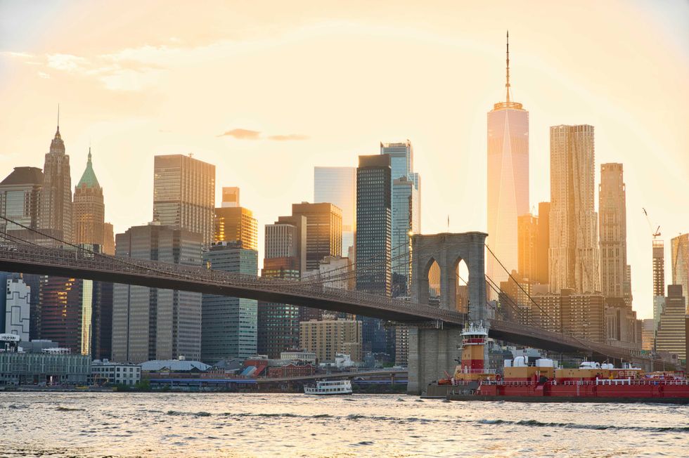 Brooklyn Bridge and NYC skyline at sunset, with boats on the East River.