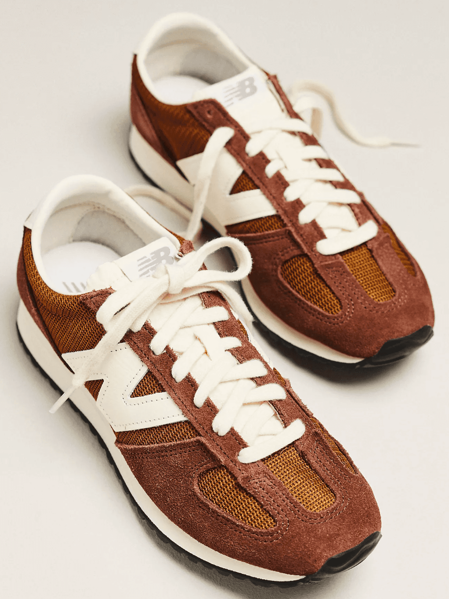 Brown and white sneakers with white laces on a plain background.