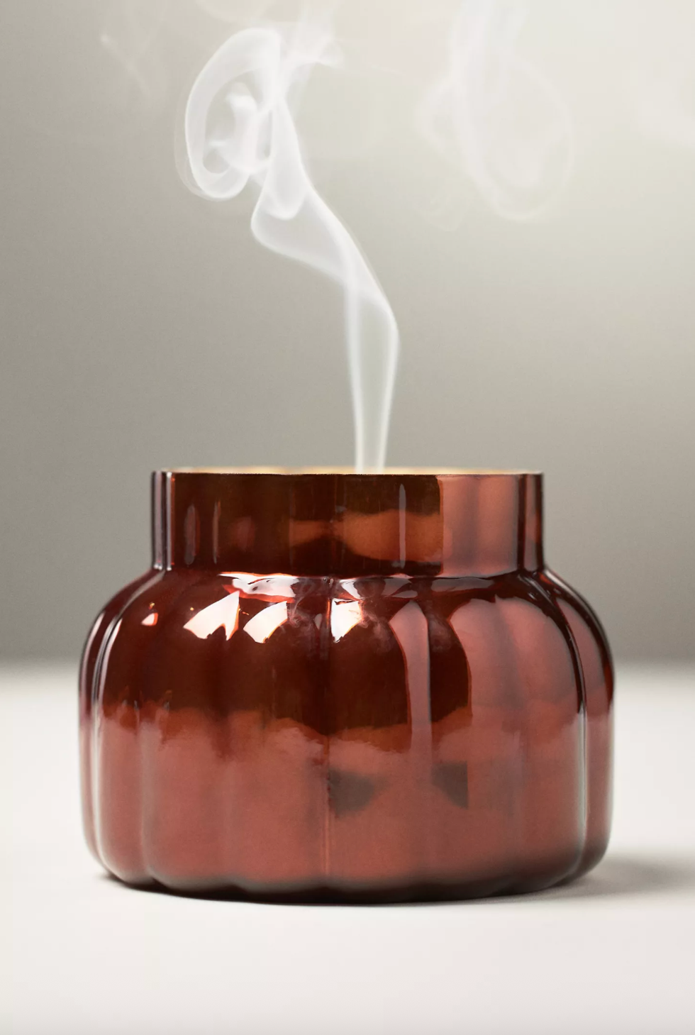 Brown glass candle jar emitting smoke.