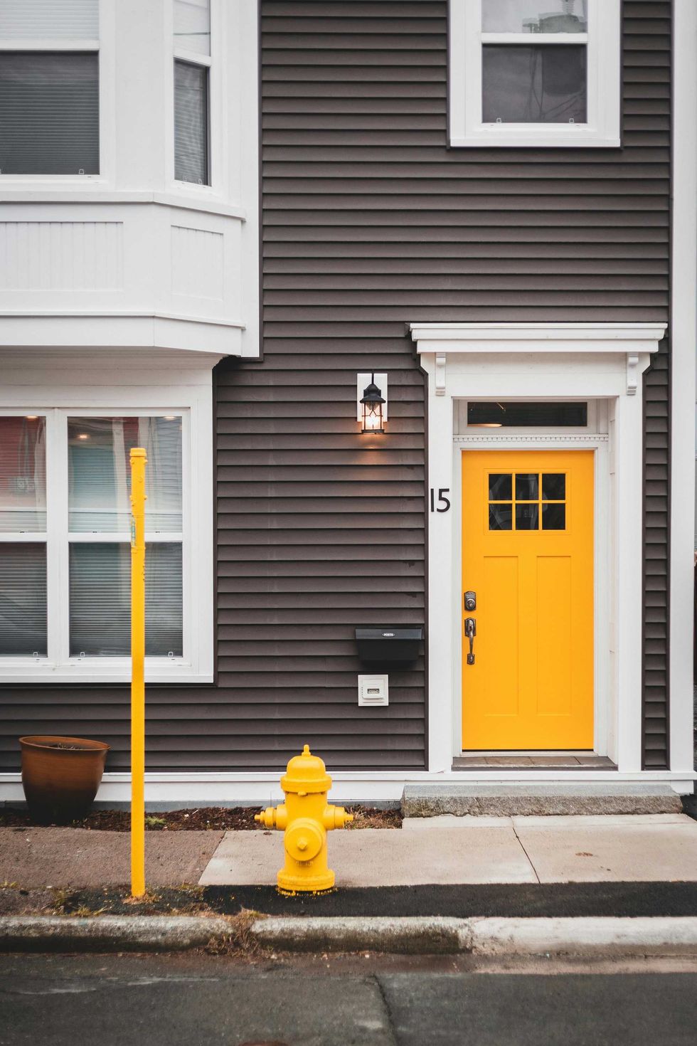 Brown house with a yellow door, hydrant, and pole, marked with number 15.