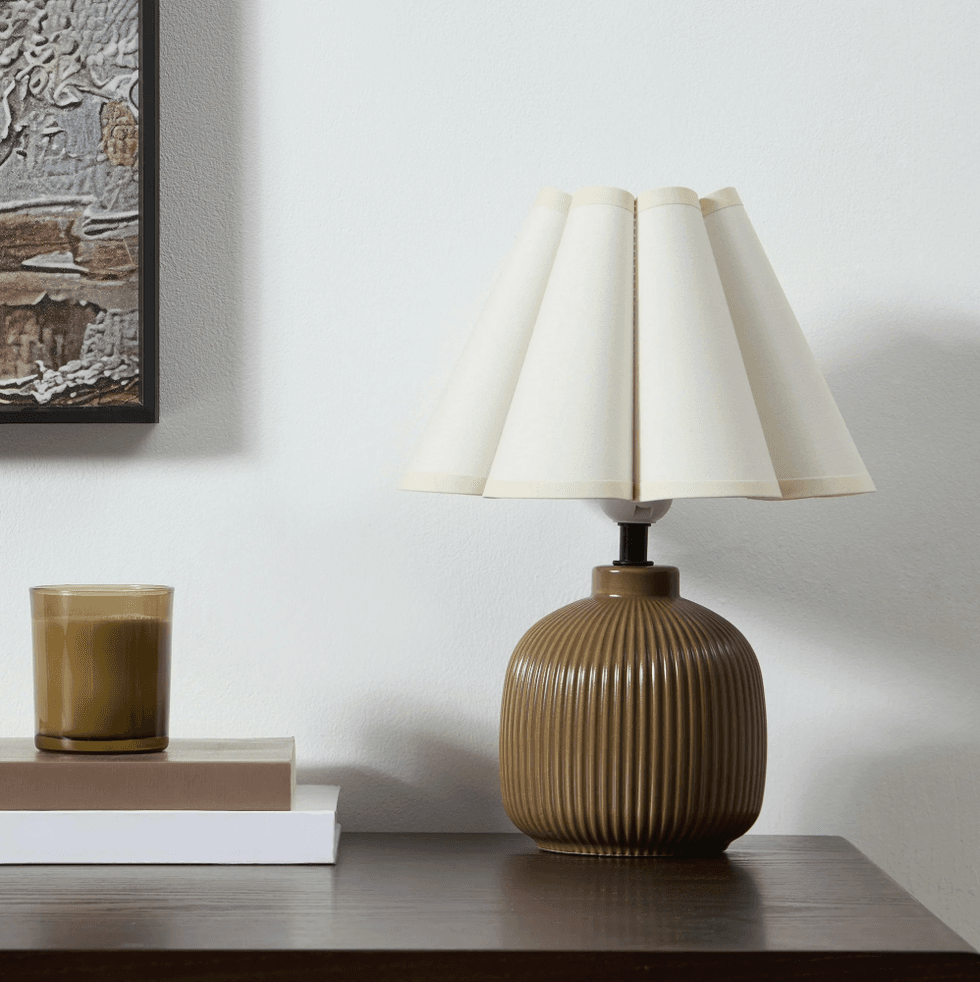 Brown lamp with fluted base beside a candle on a dark wood table.
