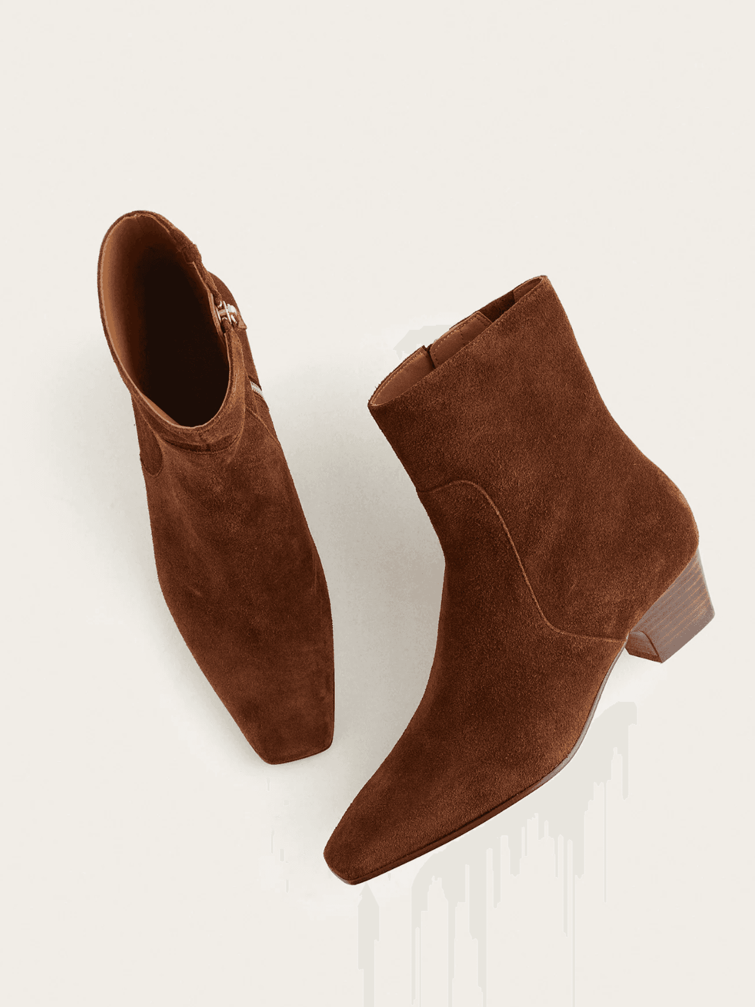 Brown suede ankle boots with low heels on a light background.