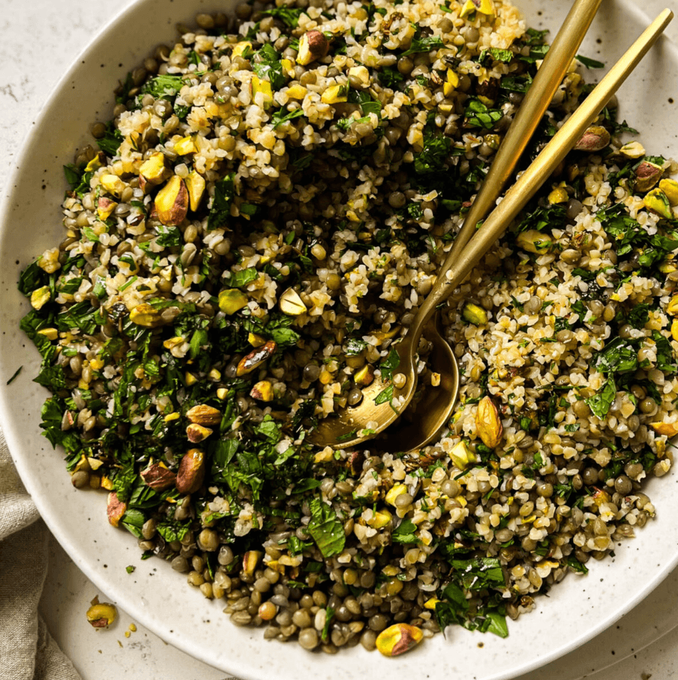 Bulgur and lentil salad with herbs and pistachios in a bowl, garnished with a spoon.