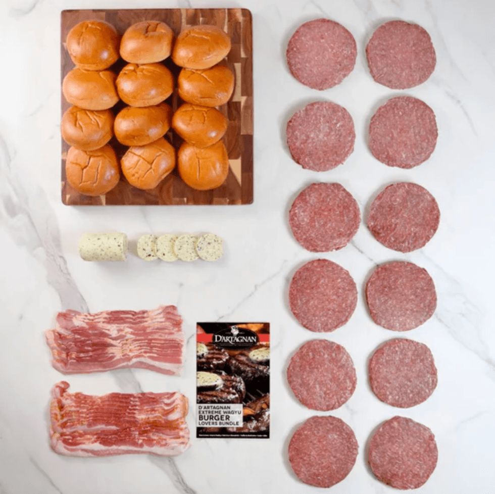 Burger ingredients arranged: buns, patties, bacon, herb butter, and a package on a marble surface.