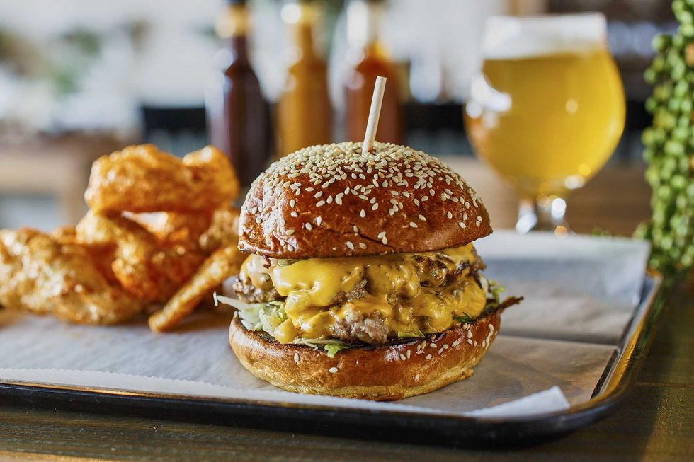 Burger with sesame bun and cheese, served with chips and a glass of beer.