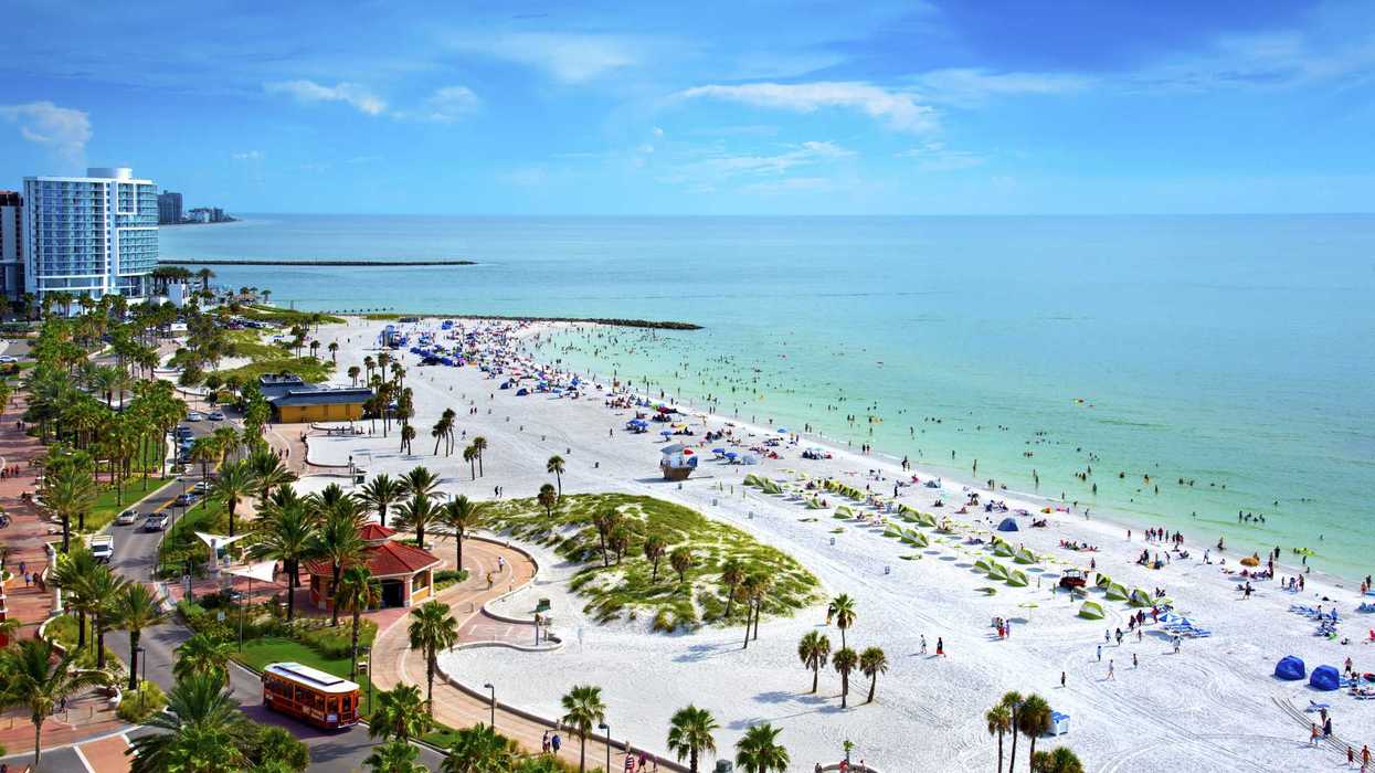 Bustling tropical beach with white sand, turquoise water, and nearby cityscape.
