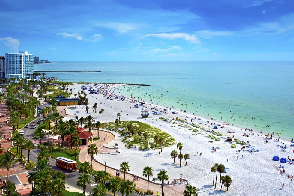 Bustling tropical beach with white sand, turquoise water, and nearby cityscape.