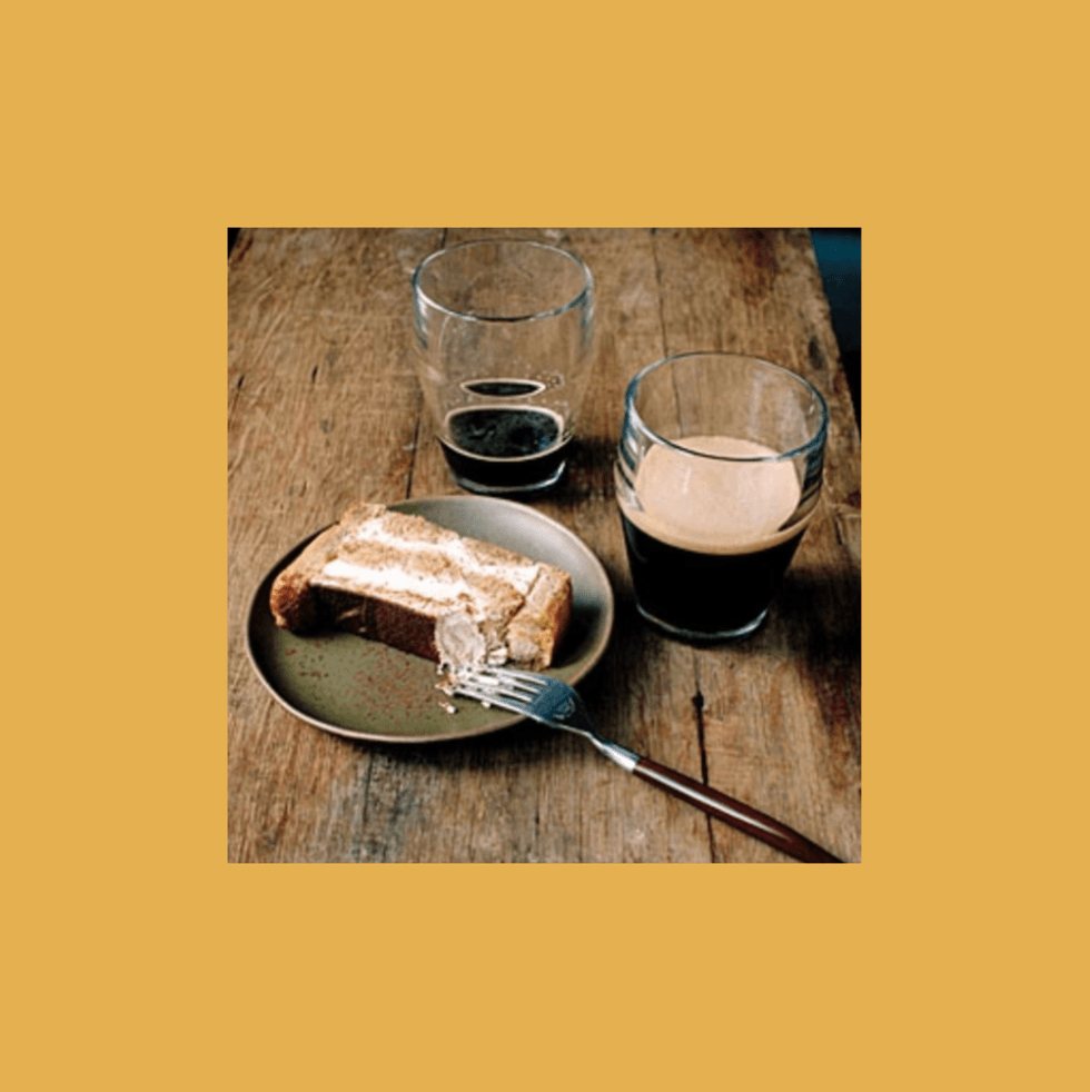 Cake slice on a plate with two glasses of dark beer on a wooden table.