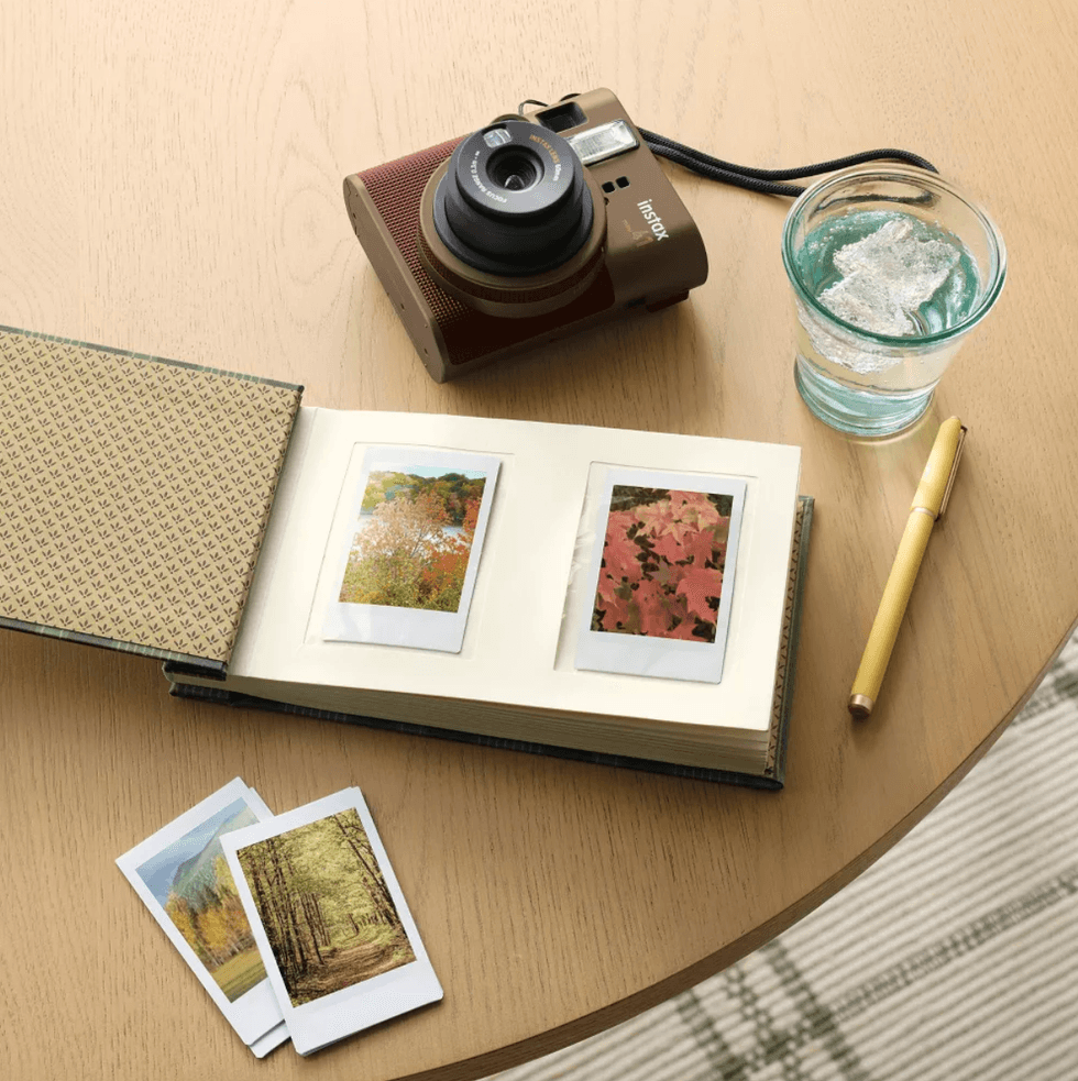 Camera, photo album, and glass on wooden table with pen.