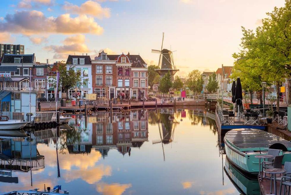 Canal scene with colorful houses, windmill, and reflections in calm water at sunset.