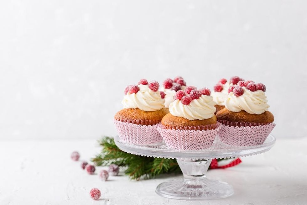 Candied cranberries and cream cheese cupcakes on glass stand. Homemade winter holiday dessert on light gray background