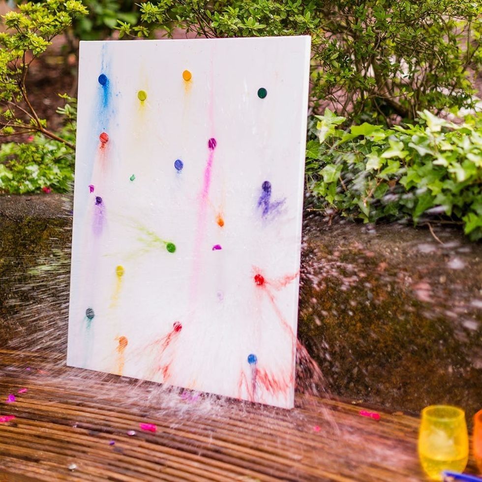 Canvas with colorful paint balloons, water bursts, on a wooden surface near green plants.