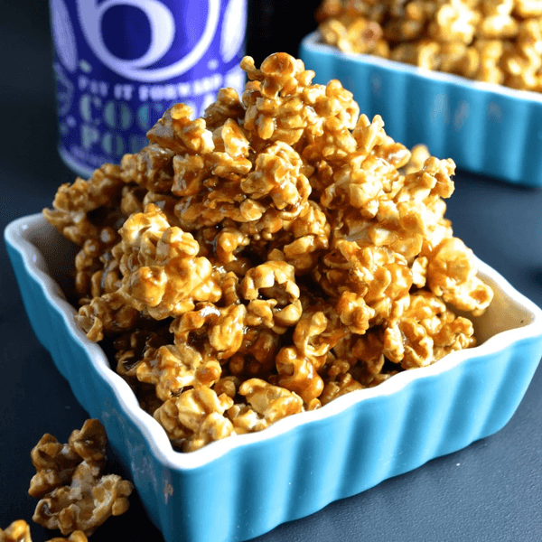 Caramel popcorn in a blue dish with a purple container nearby.