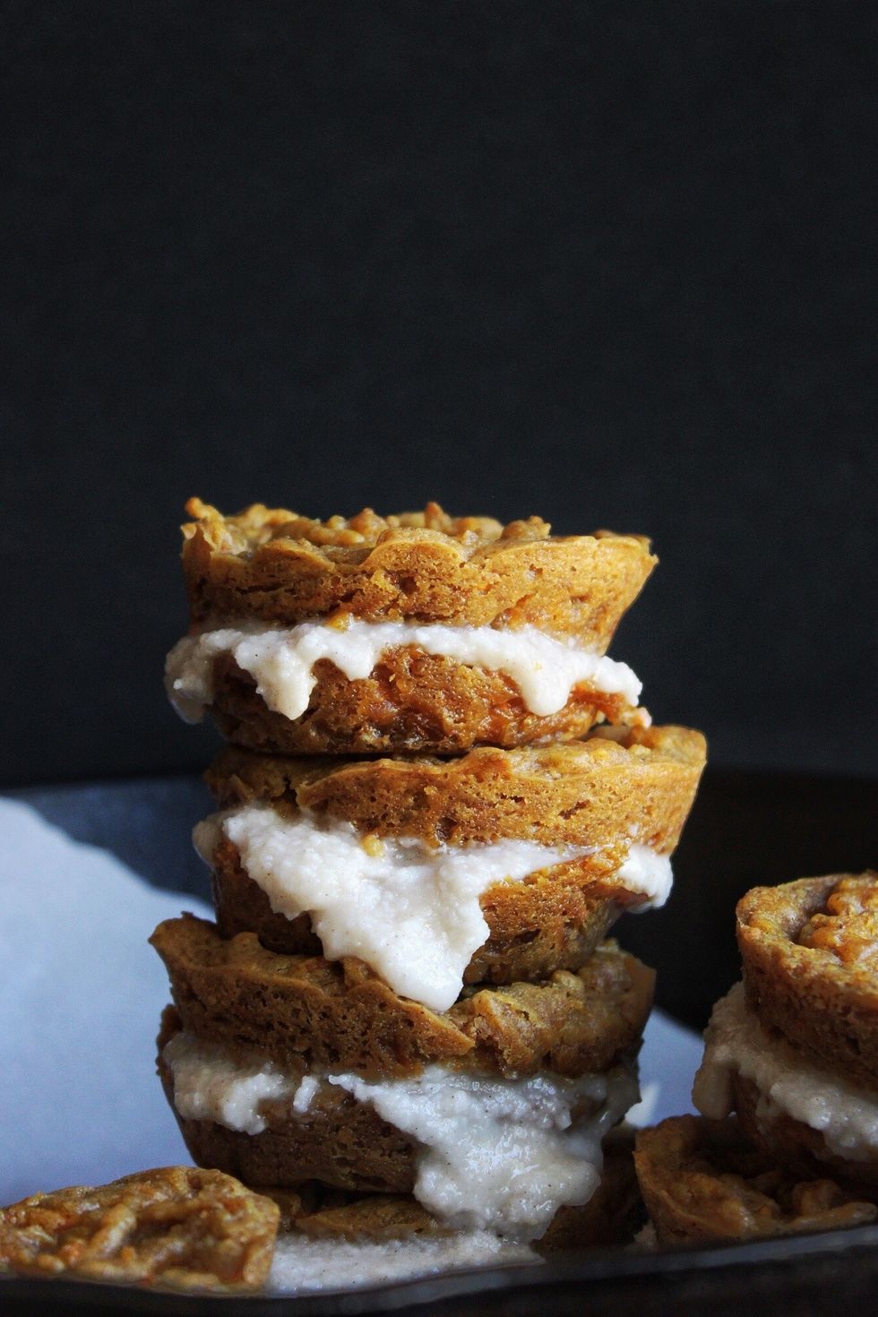 Carrot cake Whoopie Pies are stacked on top of one another in front of a black background.