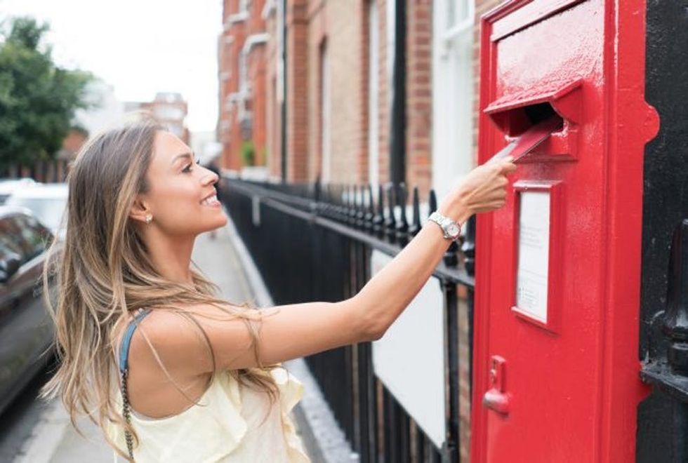 Casual woman in London sending letter through the mail and looking happy