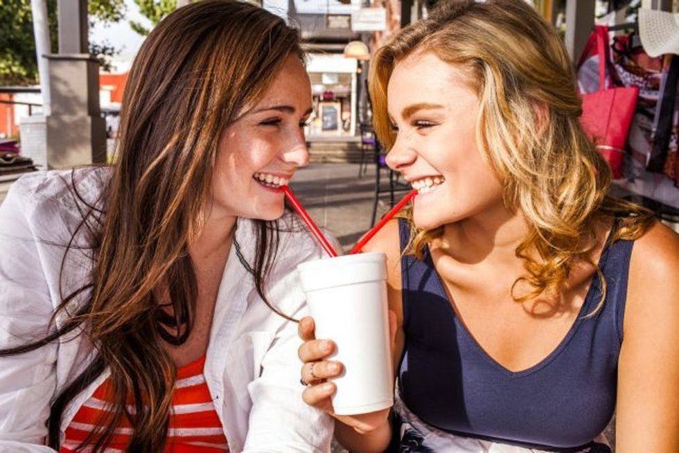 Caucasian teenage girls sharing milkshake in city