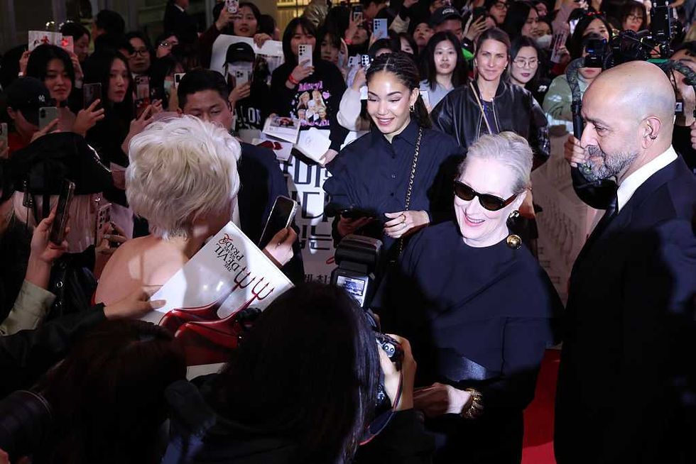 Celebrity signing autographs on a red carpet, surrounded by fans and photographers.