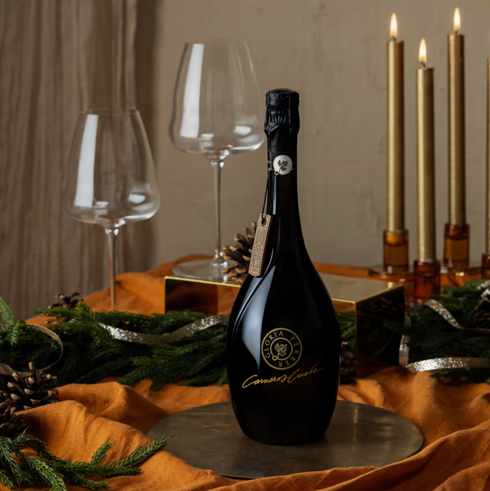 Champagne bottle on festive table with candles, glasses, pinecones, and greenery.