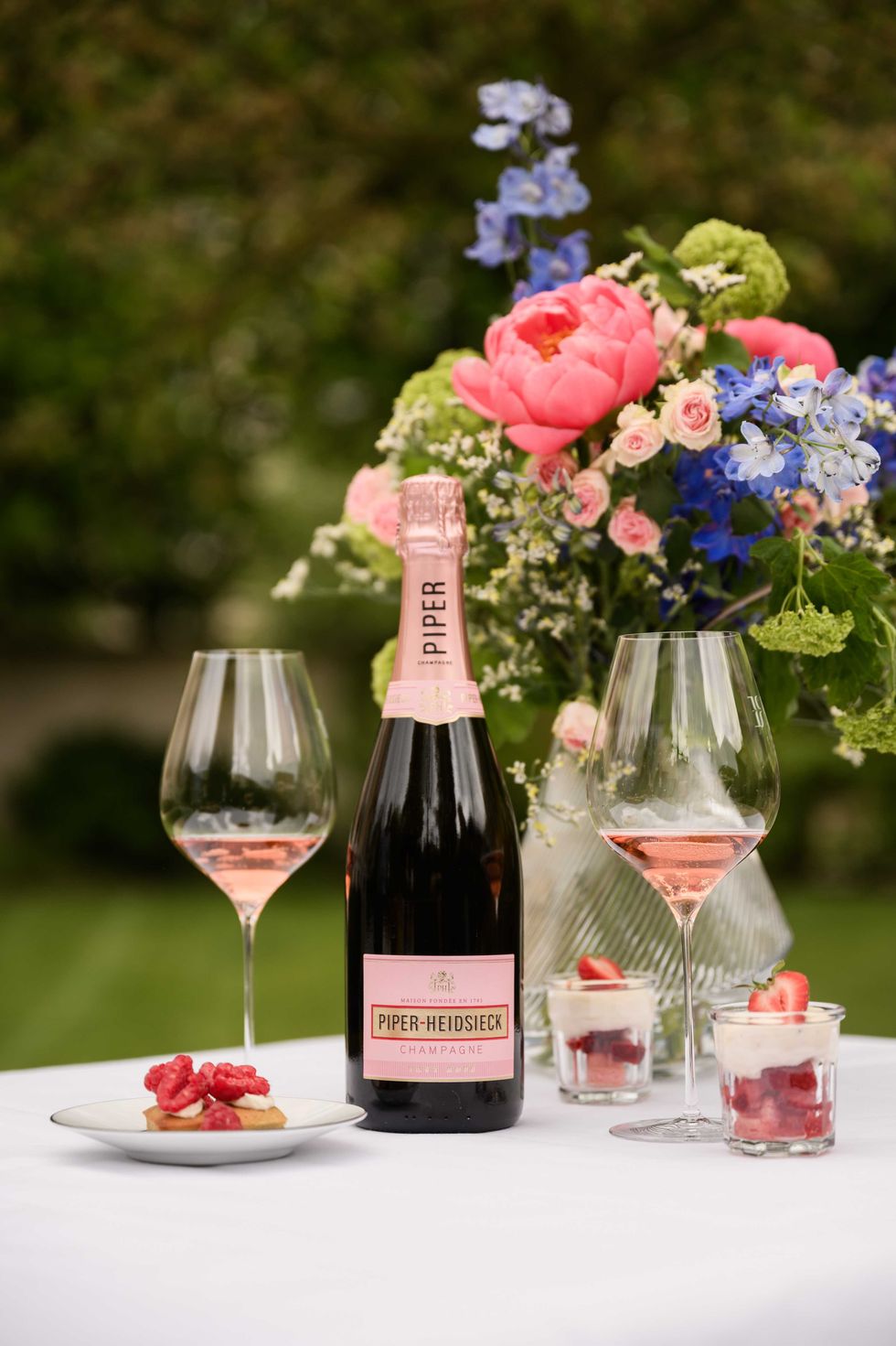 Champagne with flowers, pink glasses, and strawberry desserts on a white tablecloth.