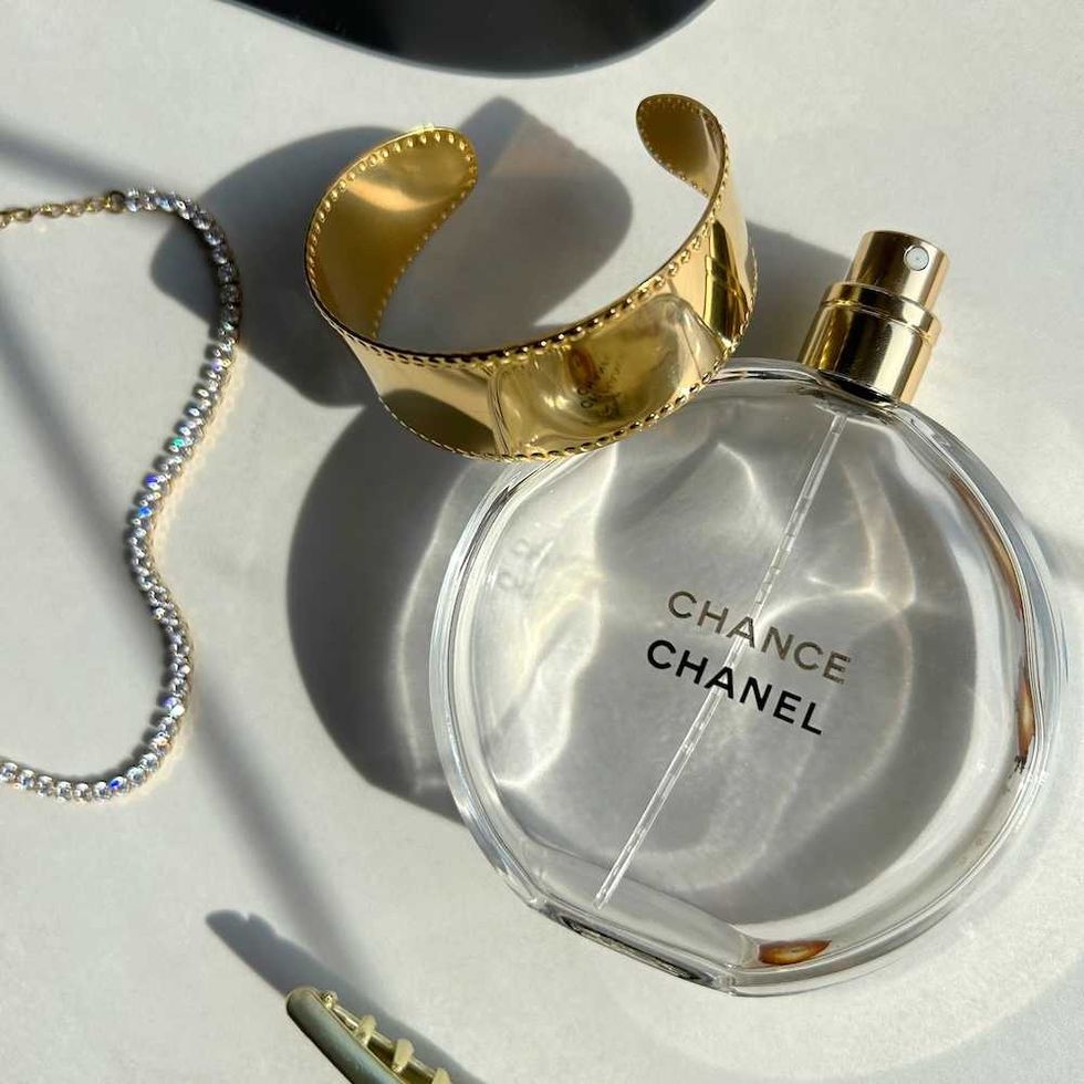 Chanel Chance perfume, gold bracelet, and rhinestone necklace on white background.