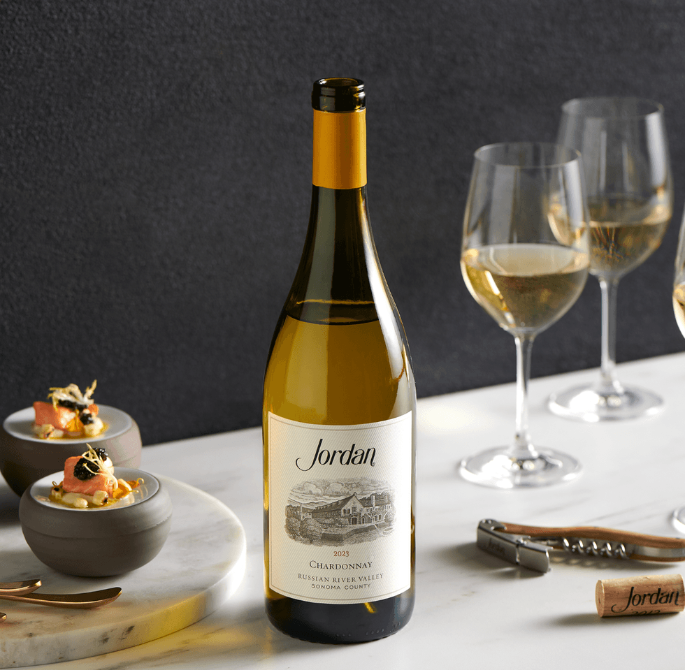 Chardonnay bottle with wine glasses and gourmet appetizers on a marble table.