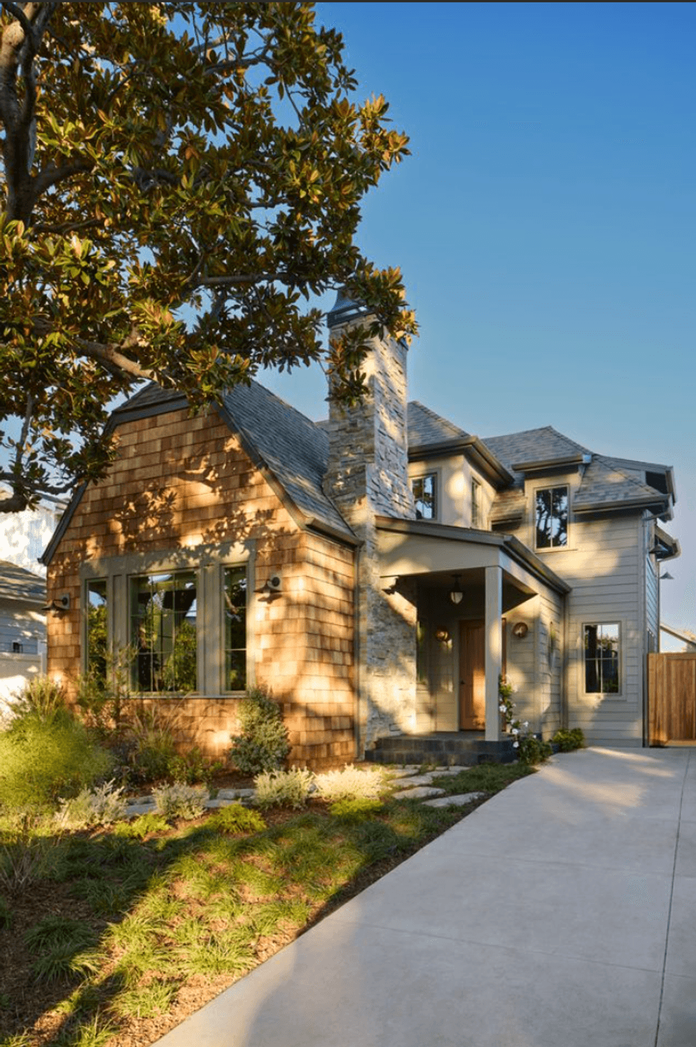 Charming two-story house with stone chimney and lush landscaping under a clear blue sky.
