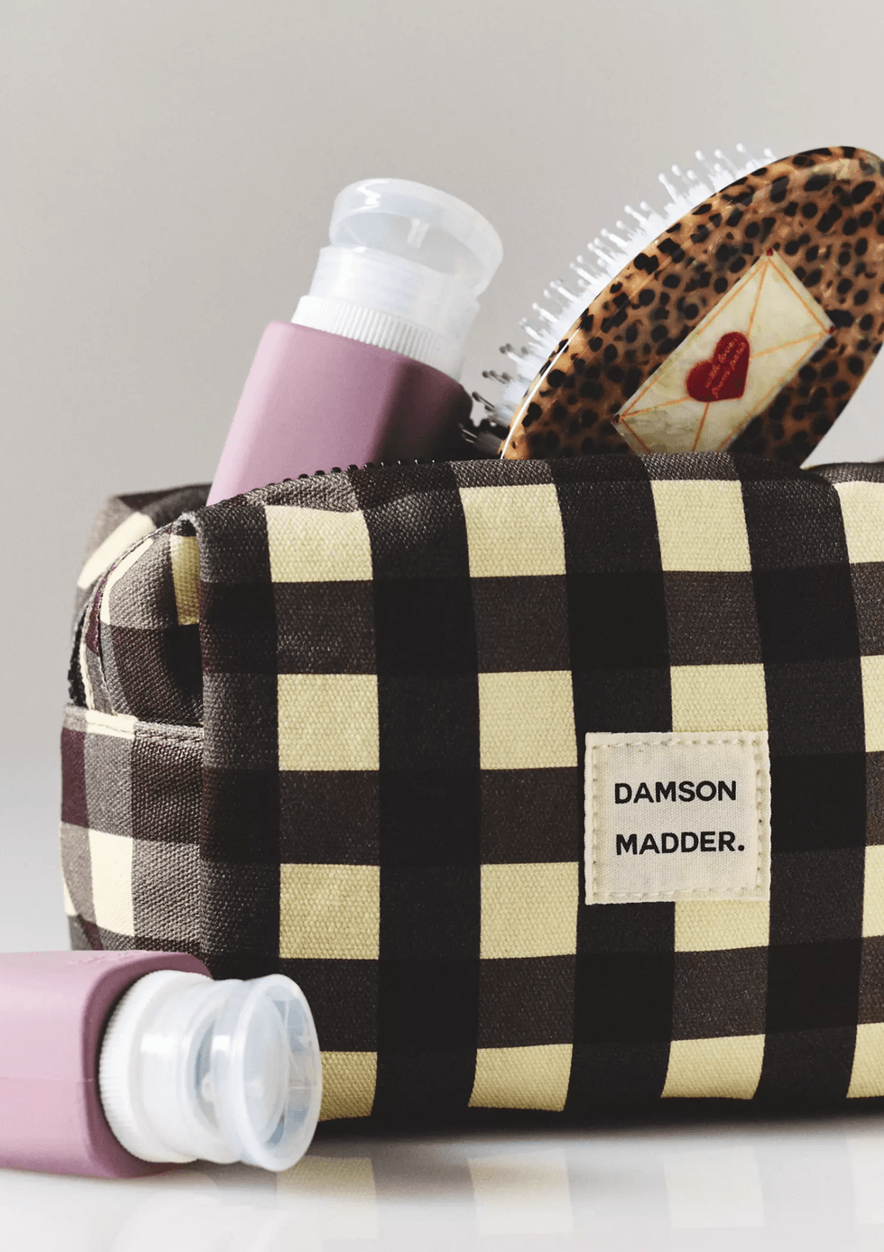 Checkered bag with hairbrush and bottle, "DAMSON MADDER" label visible.