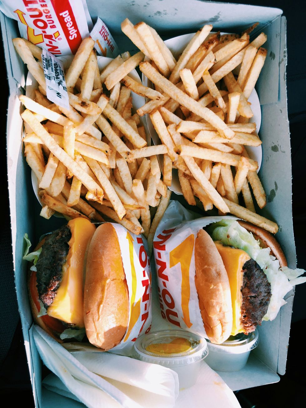 Cheeseburgers with lettuce and fries in a box, accompanied by dipping sauces.
