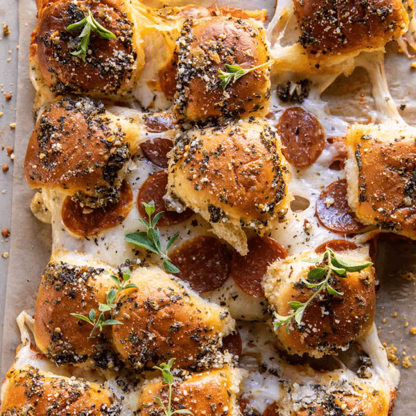 Cheesy pepperoni sliders with herbs and a glass of dipping sauce on the side.