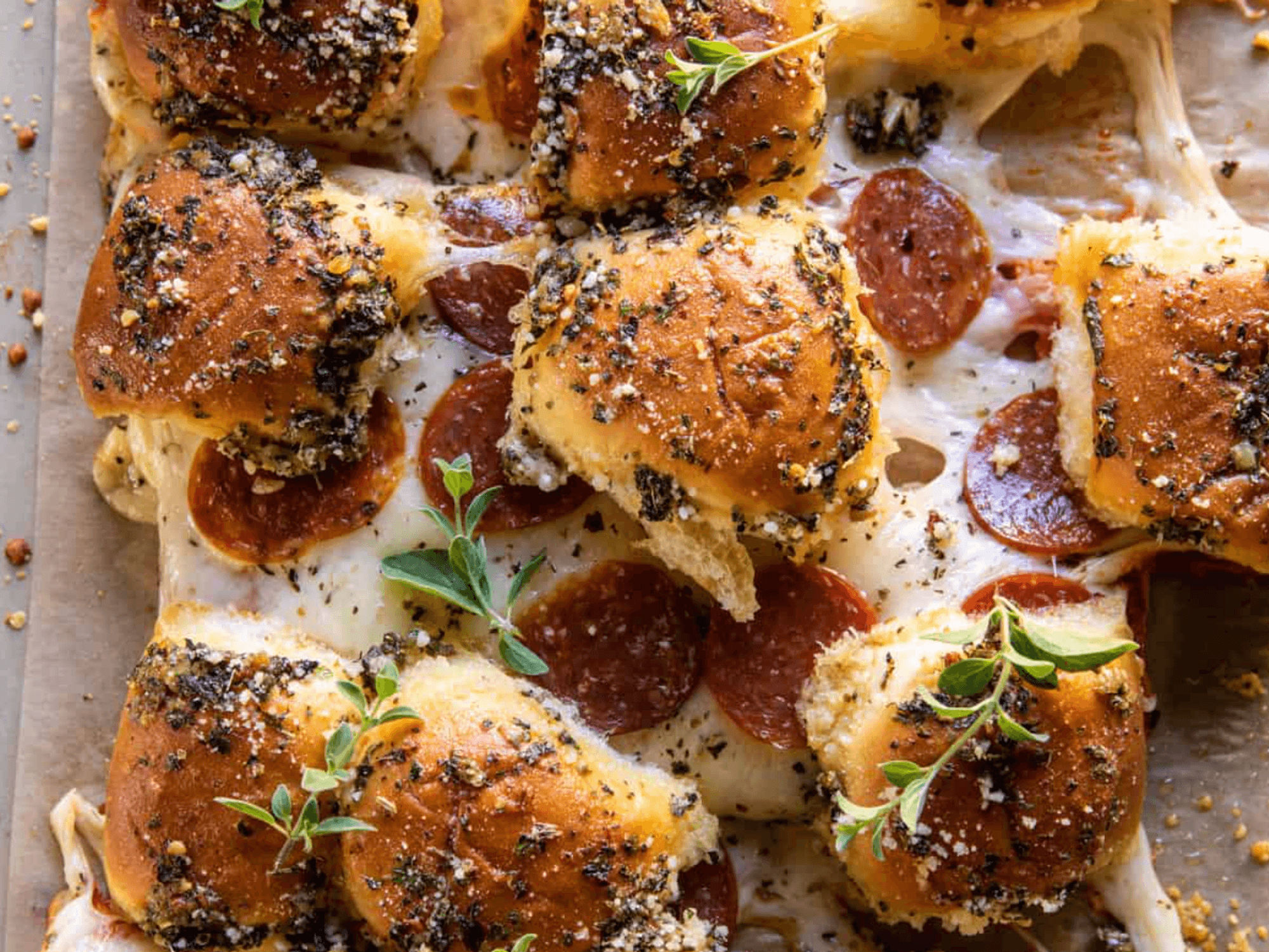 Cheesy pepperoni sliders with herbs on a tray.