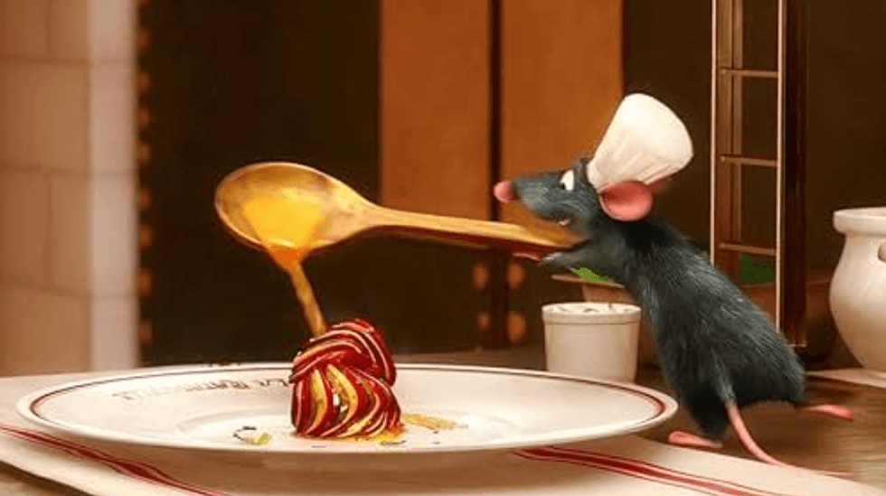 Chef rat pouring sauce on a plated dish, wearing a white hat.