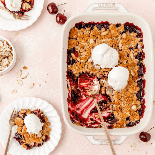 Cherry crumble with ice cream and fresh cherries on a pink background.
