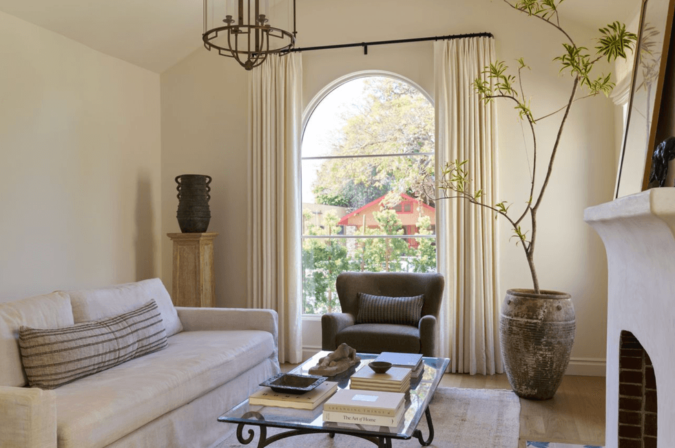 Chic living room with a sofa, armchair, large potted plant, and arched window view.