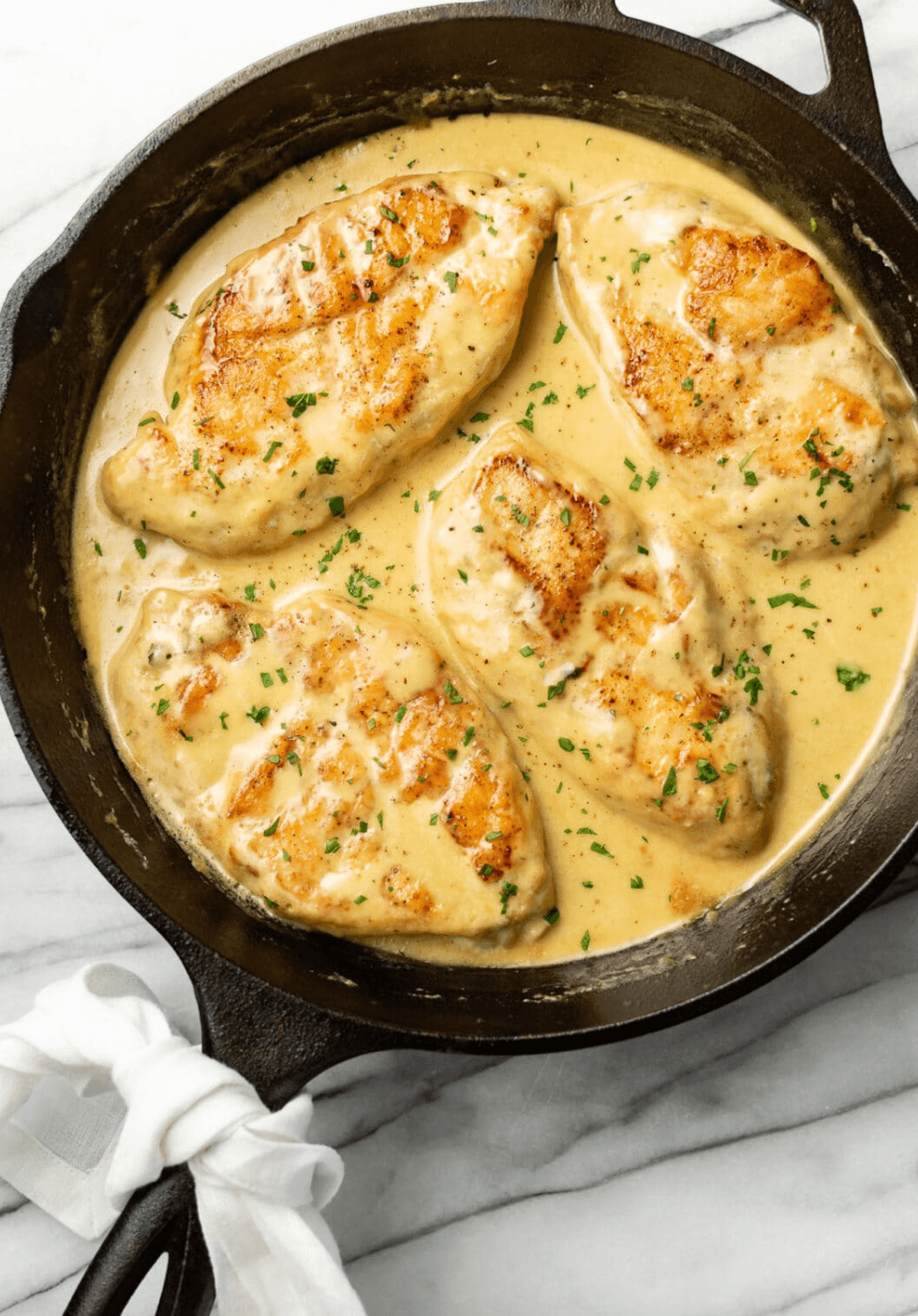 Chicken breasts in creamy sauce with herbs in a skillet.