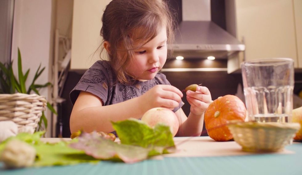 Child examining leaves and fruits at a kitchen table.