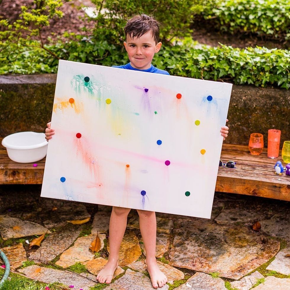 Child holding colorful canvas in garden setting.