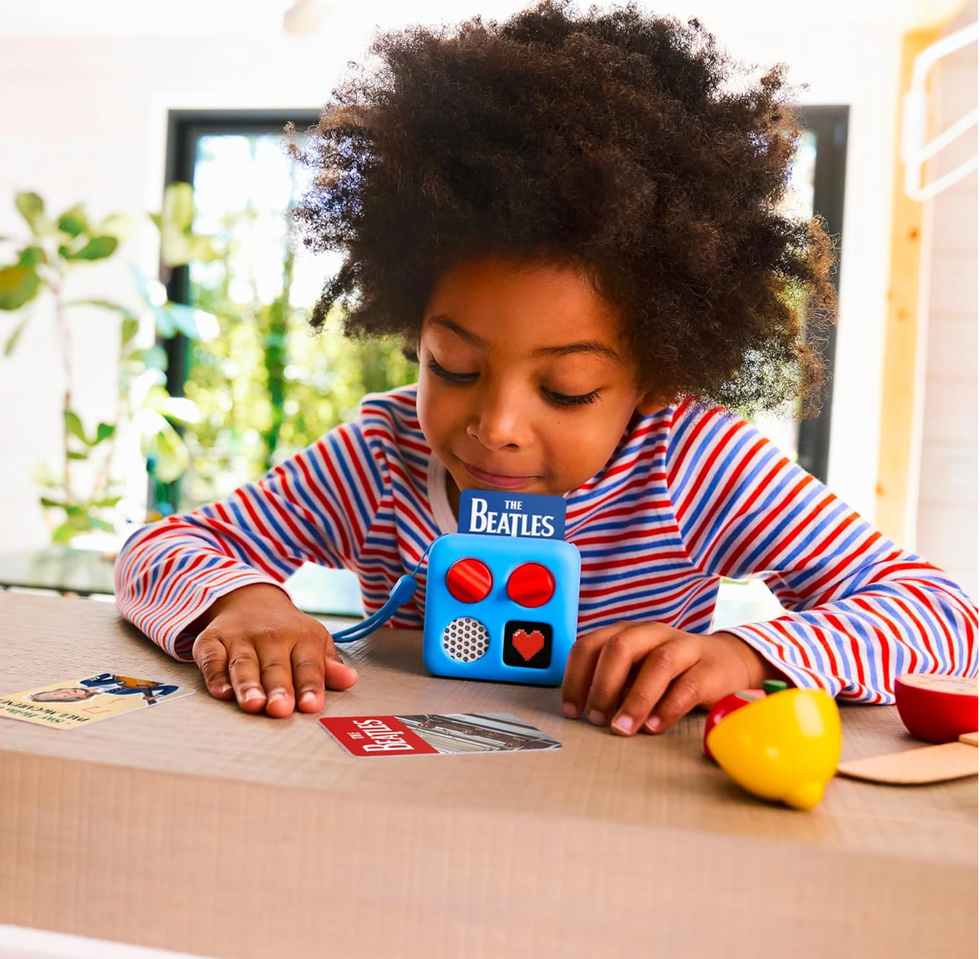 Child playing with a Beatles-themed toy on a table with various colorful objects.