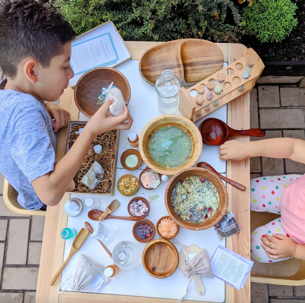 Children crafting with various colorful ingredients at a table outdoors.
