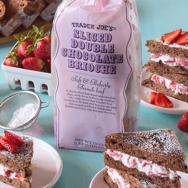 Chocolate brioche sandwiches with cream, strawberries, and sugar on a blue table.