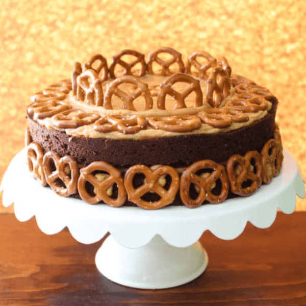 Chocolate cake decorated with pretzels on a white cake stand.