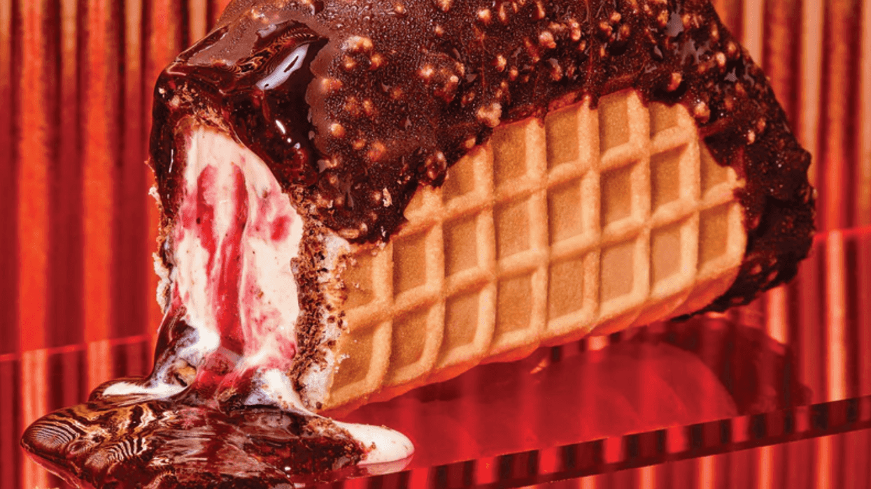 Chocolate-coated ice cream taco with raspberry filling melting on a red backdrop.
