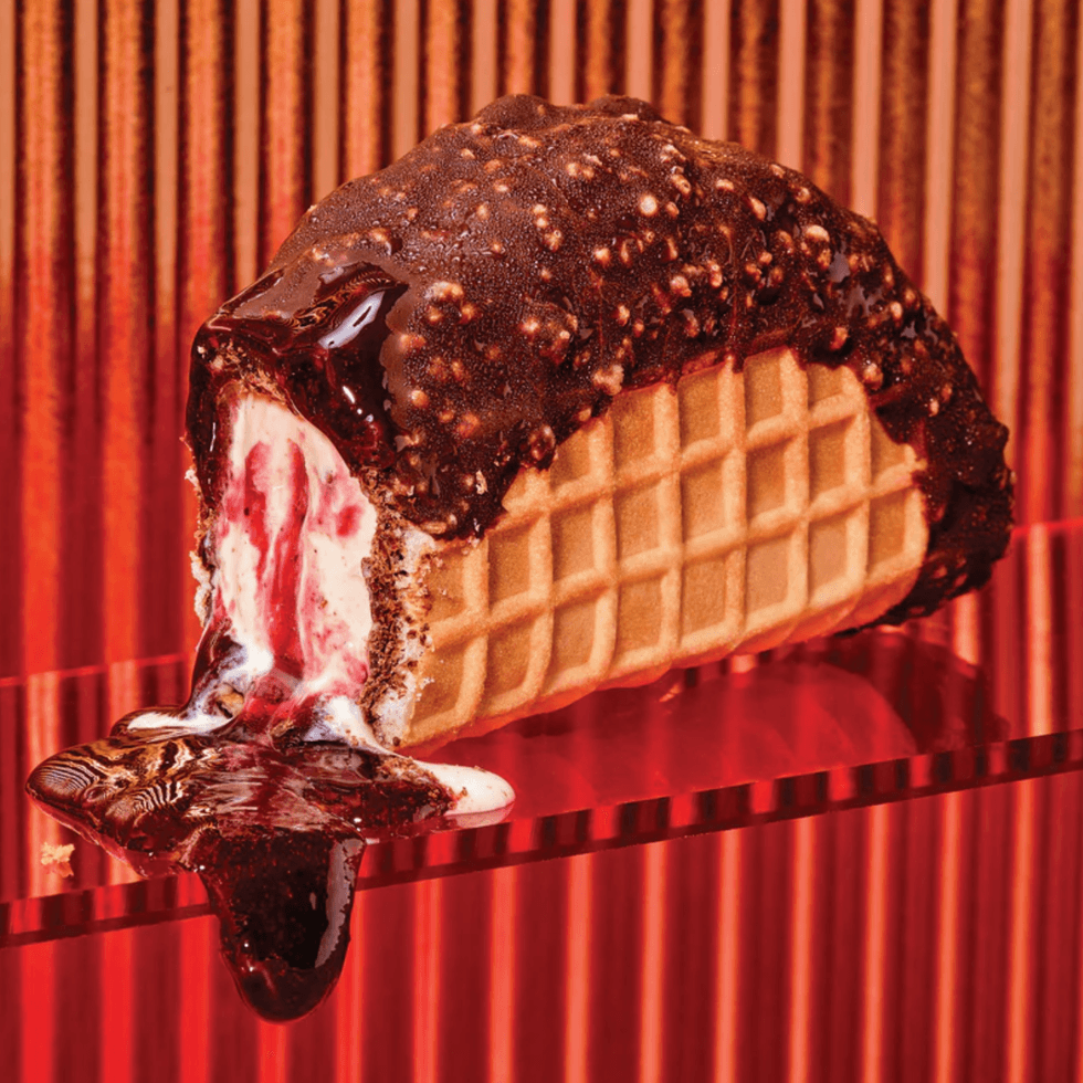 Chocolate-coated ice cream taco with raspberry filling melting on a red backdrop.