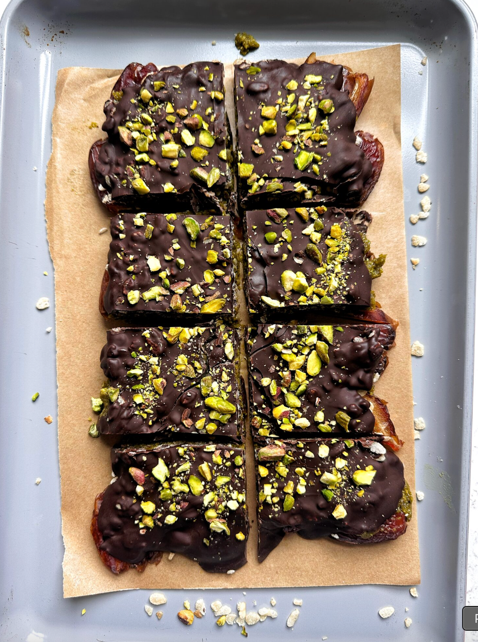 Chocolate-covered bars topped with chopped pistachios on parchment paper.