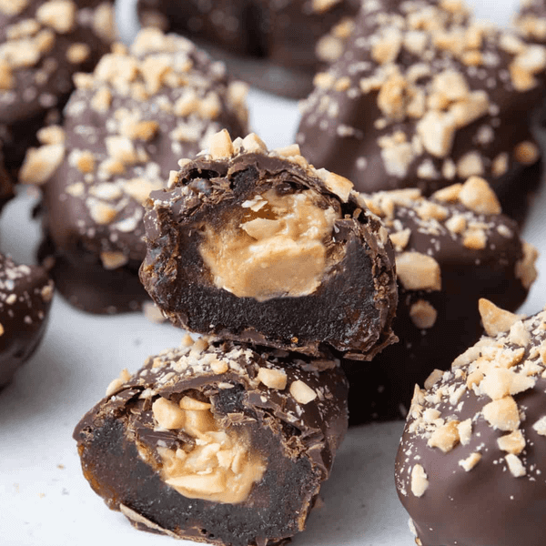 Chocolate-covered dates filled with peanut butter and topped with crushed nuts on a plate.