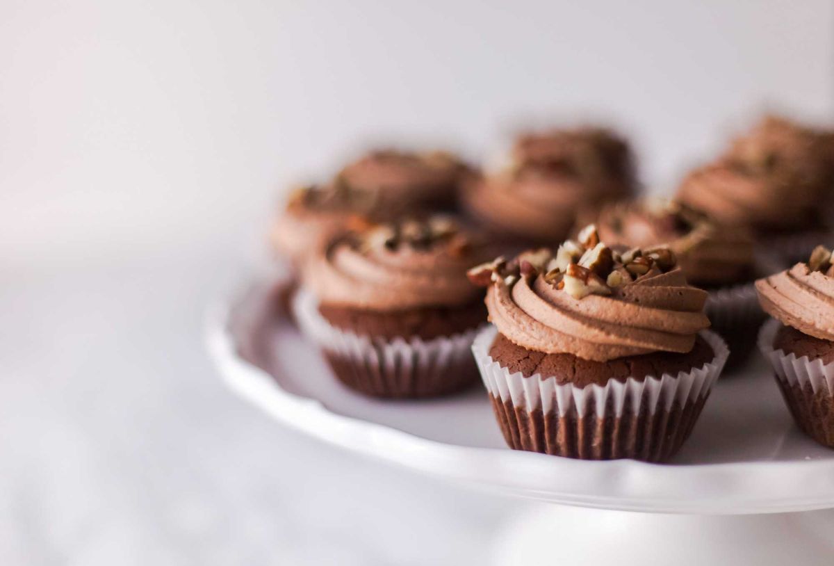 Chocolate cupcakes with swirled frosting and nuts on a white cake stand.