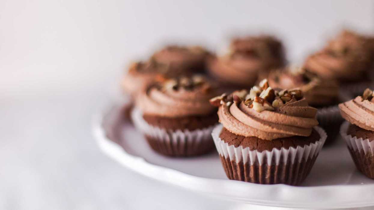 Chocolate cupcakes with swirled frosting and nuts on a white cake stand.