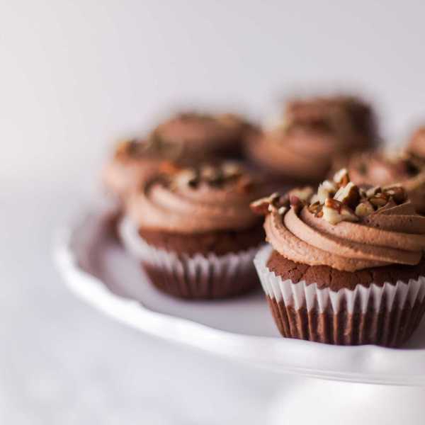Chocolate cupcakes with swirled frosting and nuts on a white cake stand.
