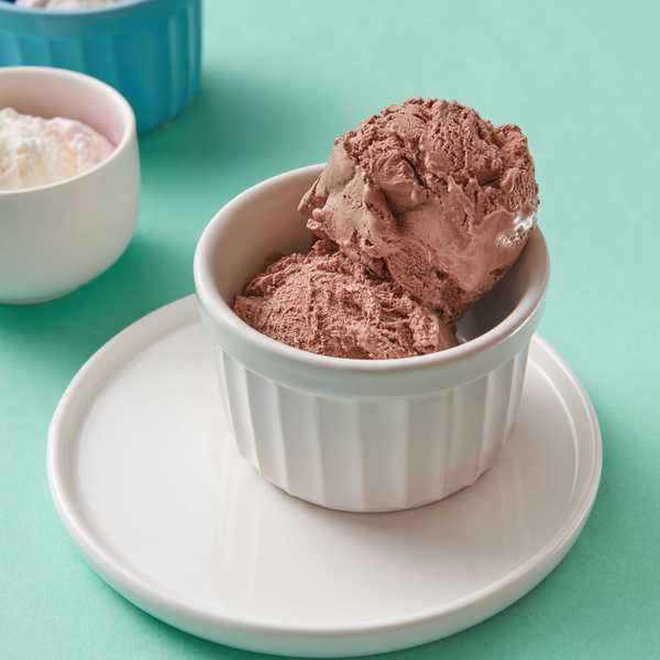 Chocolate ice cream scoops in a white ramekin on a mint green background.